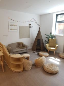 A cosy corner with cuddle sofa, an armchair and a wicker teepee in the corner. wicker basket seats and floor pads are scattered on the floor around a circular rug